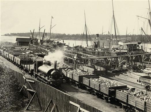 Vy över del av hamnen, där järnmalm töms från vagnar till fartyg.