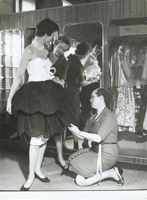 Kvinna provar klänning med assistans av måttbandsutrustad NK-personal.